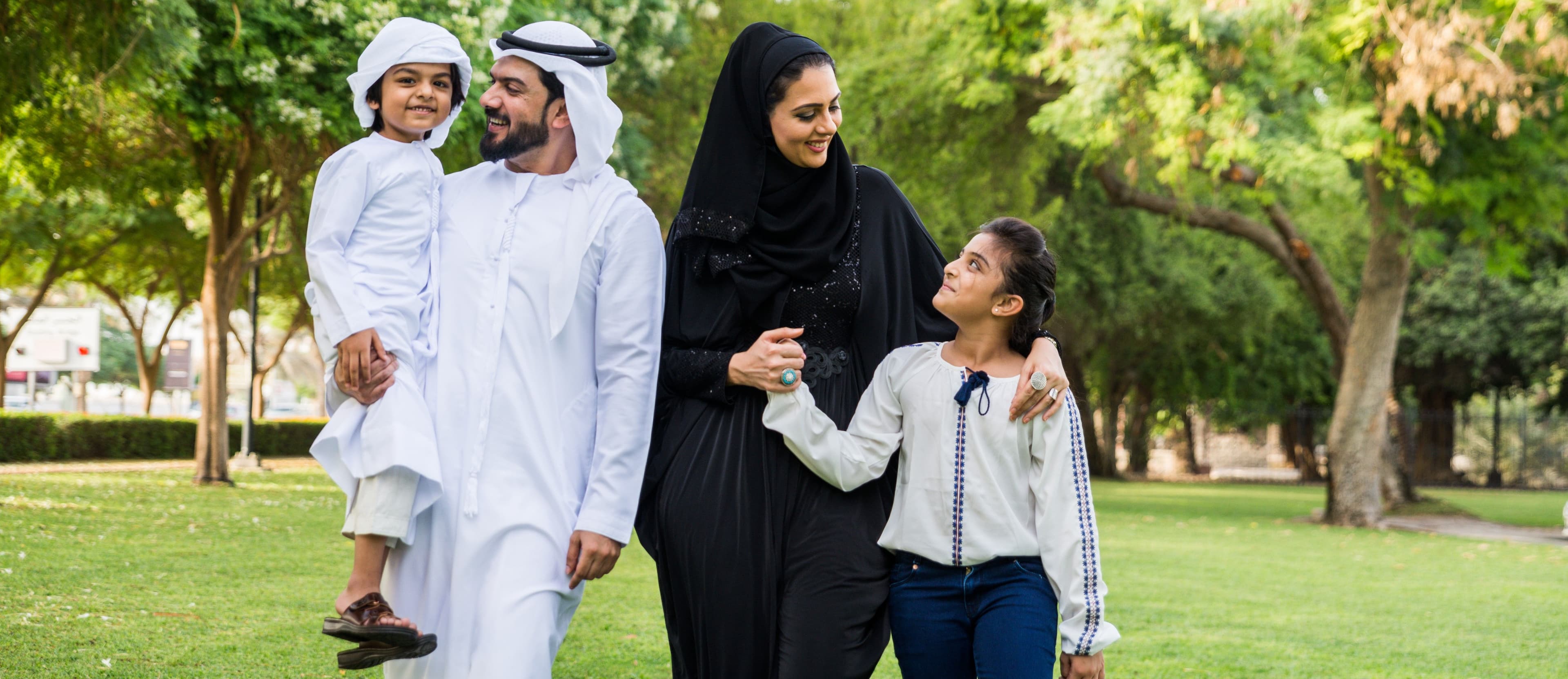 Happy Emirati family walking together in a green park in Dubai.
